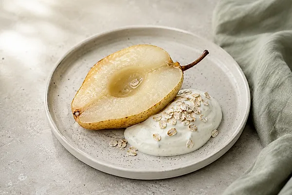 Warme, gebackene Birnenhälften mit einem Klecks Vanillequark in einer hellen Schale.