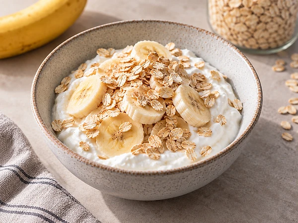 Zwei Schalen Skyr mit Bananenscheiben und Haferflocken, bestreut mit etwas Zimt.